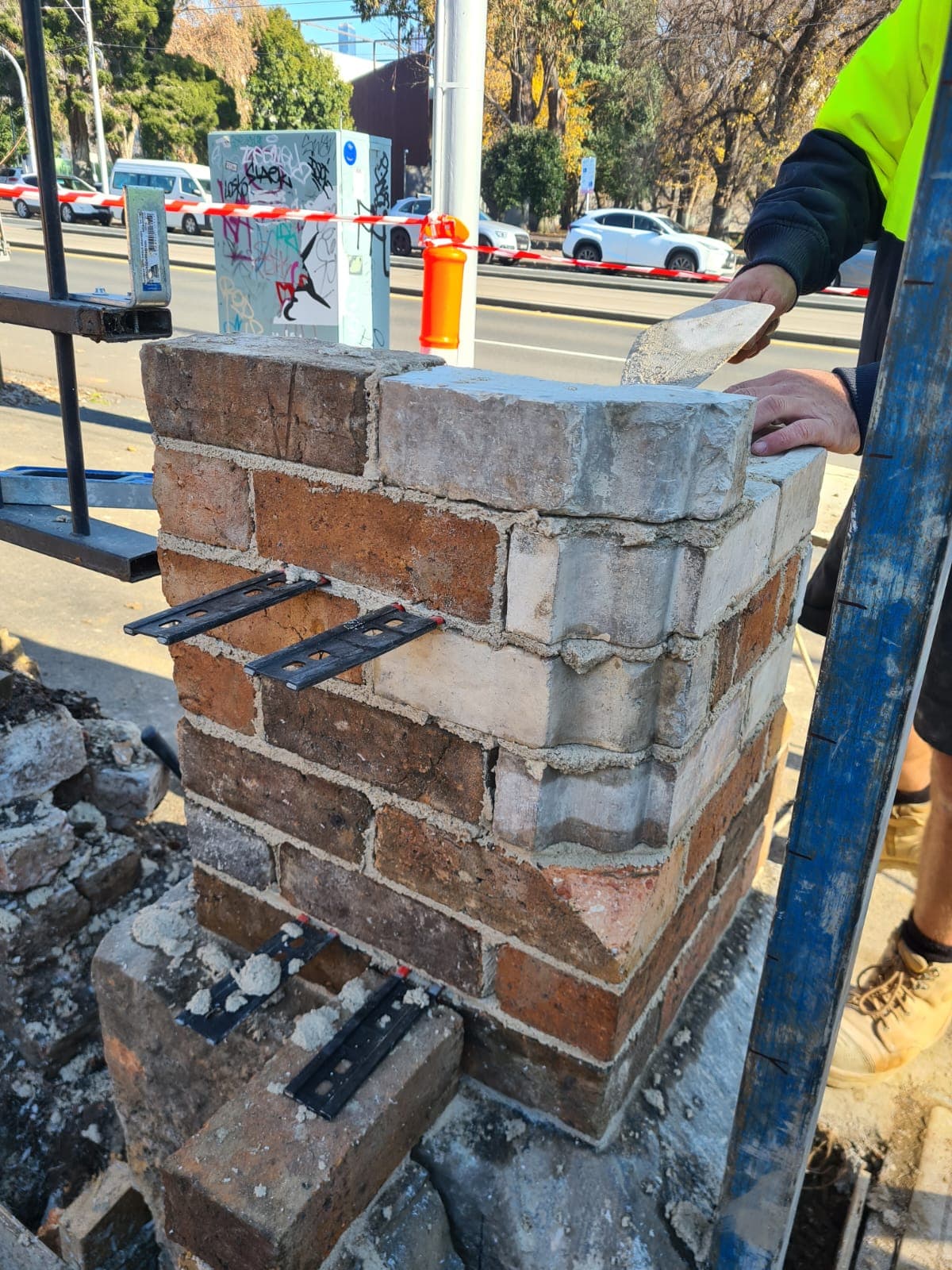 A reclaimed-brick pier being rebuilt by hand with stainless ties on the Cairo flats heritage wall